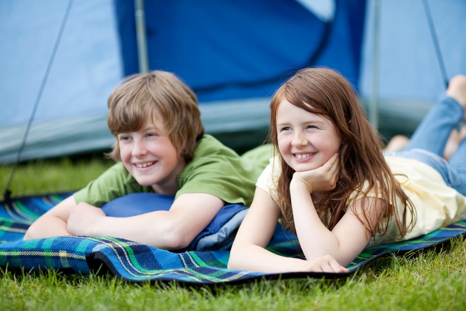 Two Kids lying on a blanket with tent in background